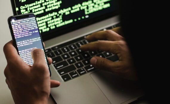 Free Unrecognizable hacker with smartphone typing on laptop at desk Stock Photo