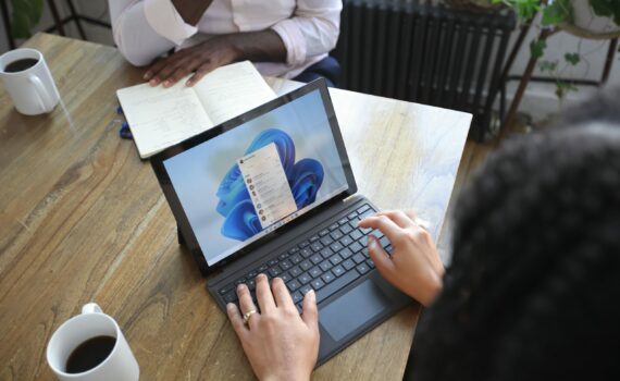 Overhead view of two people at a table working with a Microsoft laptop and notebook